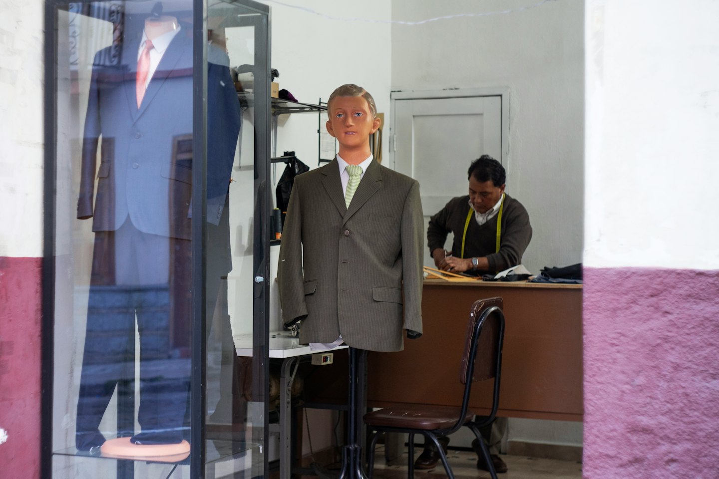 Tailor cutting fabric with measuring tape around neck.