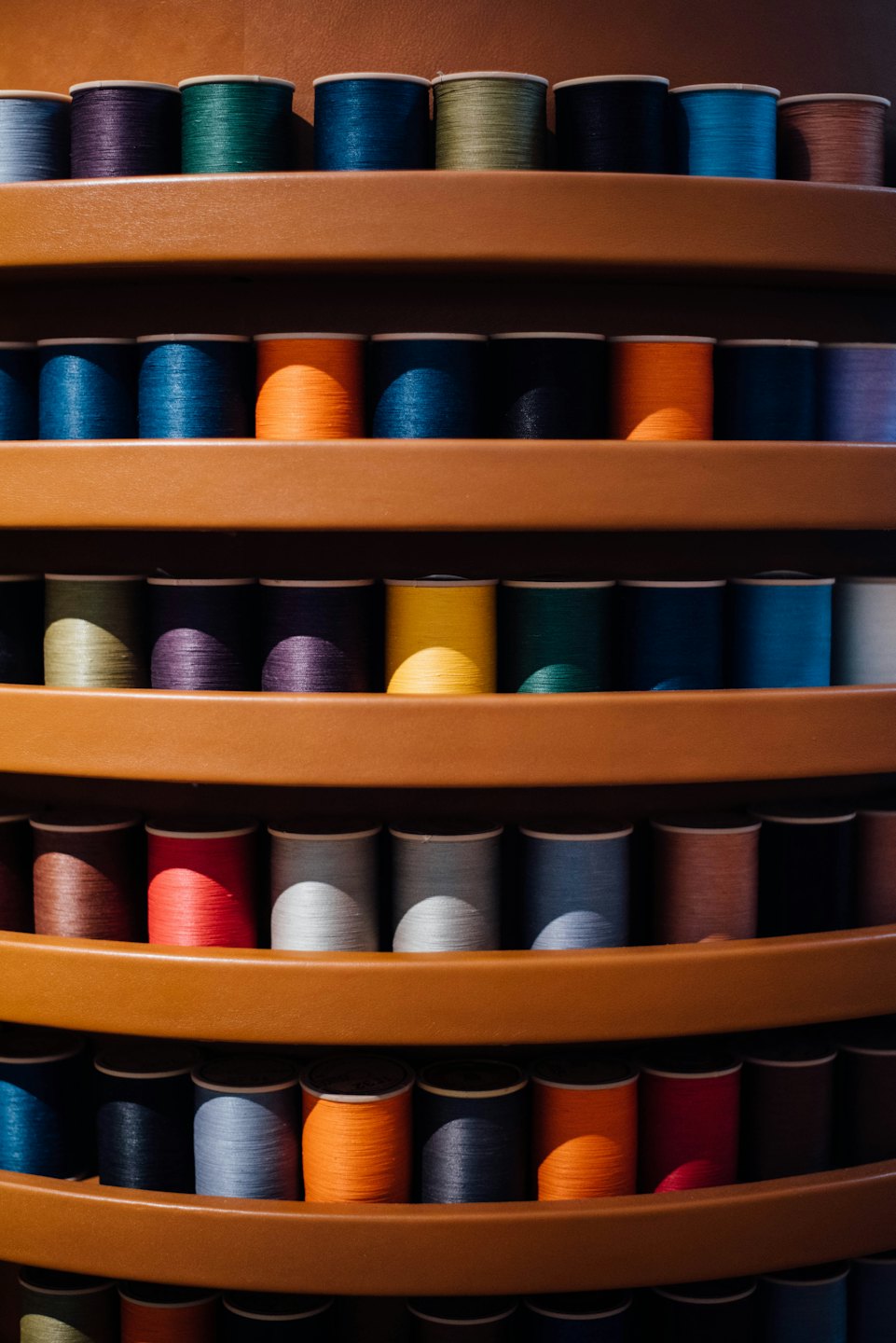 Colorful spools of thread arranged on curved wooden shelves.