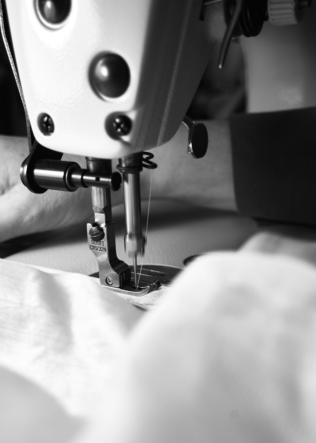 An industrial sewing machine needle stitches through white fabric.