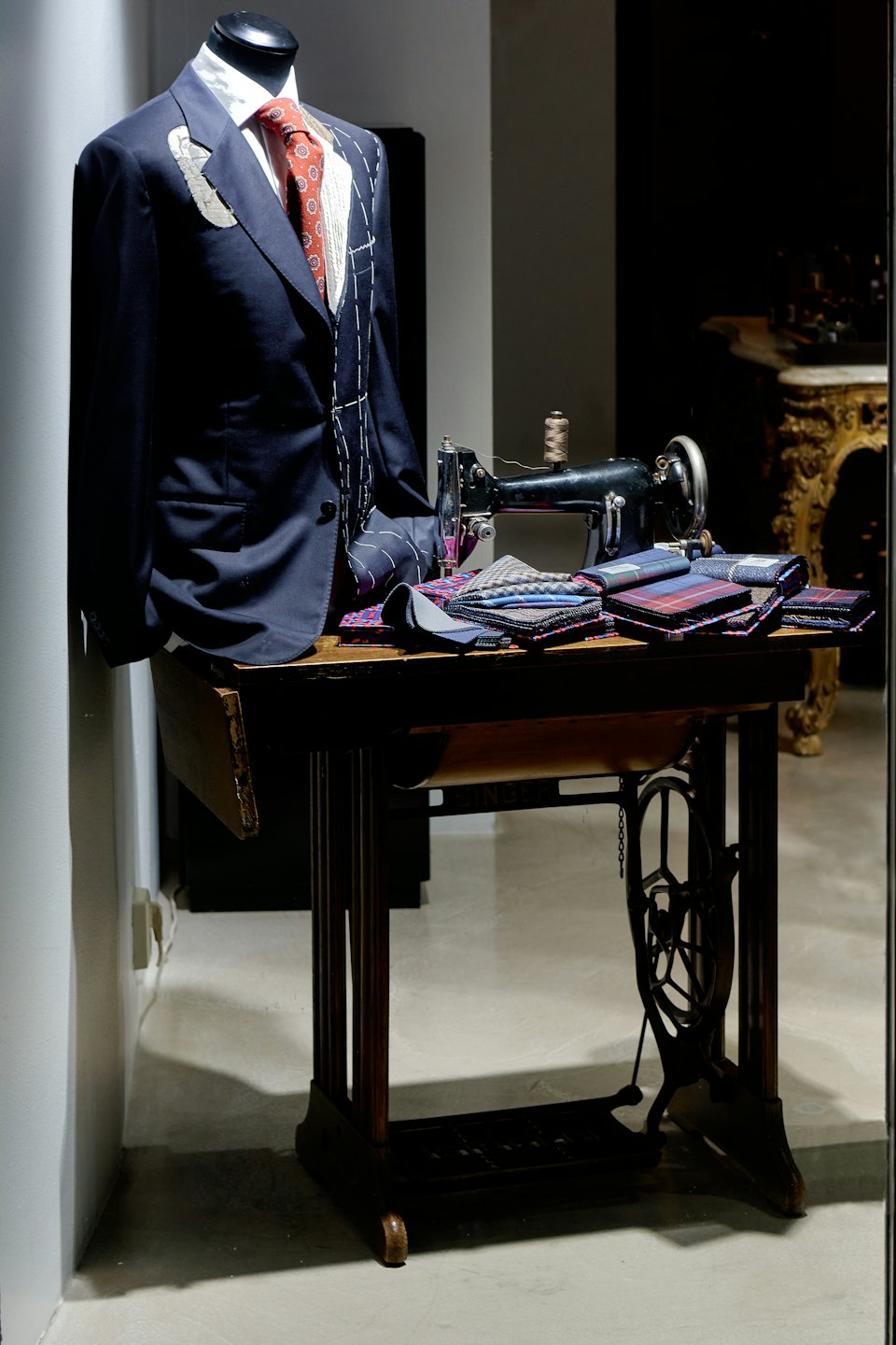 Navy suit jacket with chalk marks on a mannequin near sewing machine.