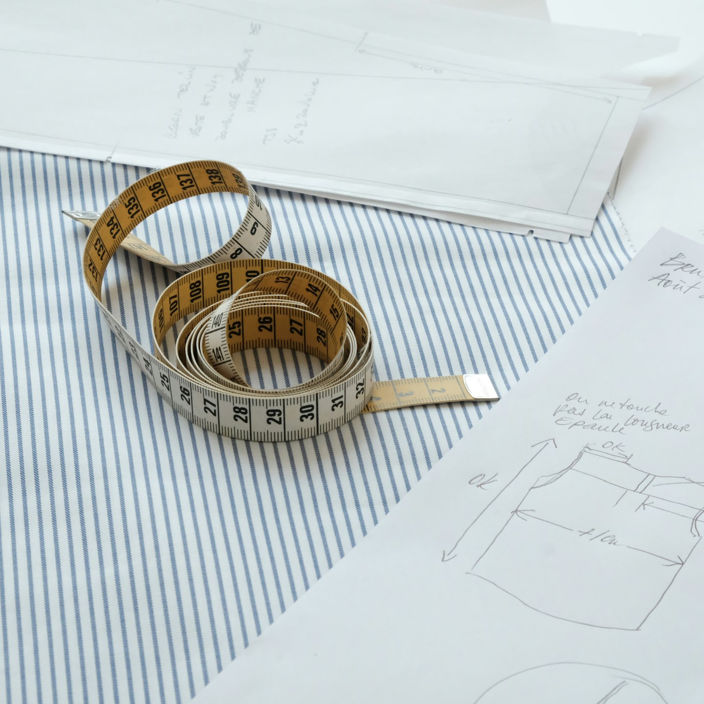 Tailor's desk with fabric, measuring tape, and French design sketches.