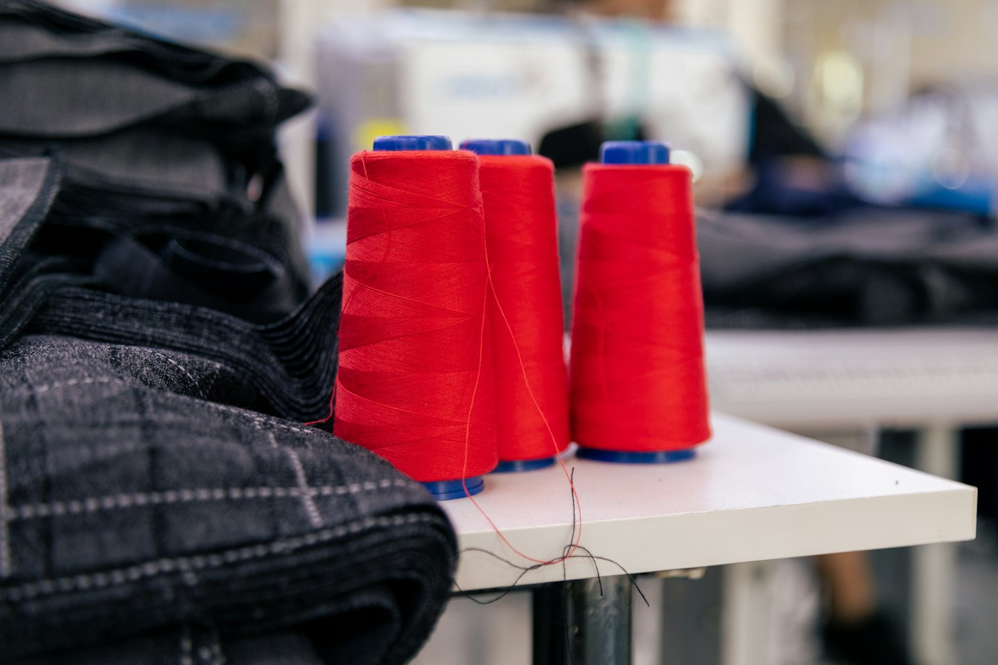 Three red spools of thread and grey fabric on a white table.